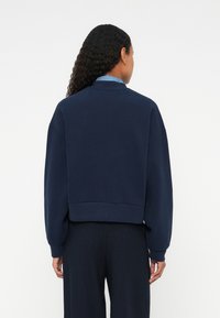 Námornícky modrý skrátený sweatshirt z jemnej látky, s okrúhlym golierom a spustenými ramenami. Hladká textúra s rebrovanými manžetami a spodným lemom.