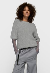 Pull en maille gris clair avec un col rond et des manches bouffantes, associé à un pantalon gris clair doté d'une ceinture noire et d'accents logo.