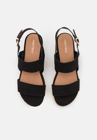 Sandalias de ante negro con dos correas anchas, hebilla ajustable en el tobillo y suela de yute en cuña. El forro interior es de color marrón claro.