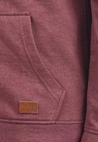 Sudadera burdeos con un tejido texturizado, bolsillo tipo canguro y una etiqueta de cuero marrón con la palabra "BLEND" grabada. Dobladillo y puños acanalados.