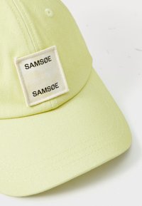 Berretto da baseball verde chiaro con una toppa rettangolare bianca che presenta il nome del marchio "SAMSØE" stampato due volte in nero.