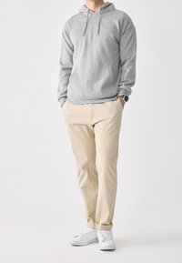 Felpa grigia con tasca a marsupio, pantaloni beige e scarpe da ginnastica bianche. La felpa presenta un cordoncino e polsini a coste.