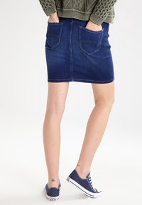 Jeanskjol i mörkblått med två baktill fickor och en åtsittande silhuett, matchad med blå kanvas sneakers.