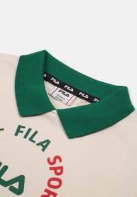 Polo beige con colletto a coste verde, caratterizzato da un marchio FILA rosso e verde. Realizzato in tessuto morbido con un design classico.
