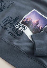 Hall gray sweatshirts, mille ehitise foto print, kihilisest tekstigraafikast ja tekstuuriga kangast varrukatel ja allservas.