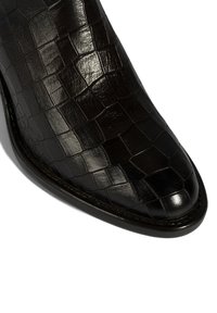 Schwarzer Leder-Stiefelette mit strukturierter, krokodilgeprägter Optik. Verfügt über eine spitze Schuhspitze und glänzendes Finish. Nahtverlauf entlang der Sohle sichtbar.