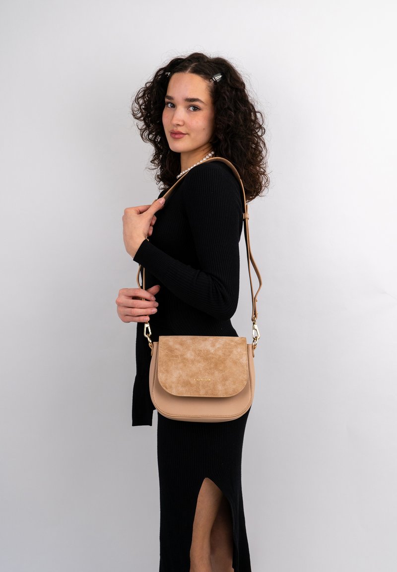 Borsa a tracolla beige con pattina in suede, corpo in pelle liscia, accessori in oro e una lunga tracolla regolabile, mostrata su uno sfondo neutro.