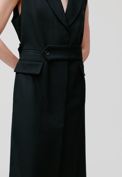 Zwarte mouwloze vest met een op maat gemaakte ontwerp, uitgerust met een tailleband, twee voorzakken en een V-hals. Gemaakt van gestructureerde stof.