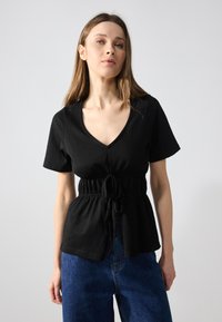 Black short-sleeve top with a V-neck and an adjustable drawstring waist. Soft, smooth fabric with a fitted bodice and relaxed fit.