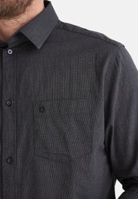 Schwarzes gemustertes Hemd mit Button-Down-Kragen, einer einzelnen Brusttasche und strukturiertem Stoff. Verfügt über passende Knöpfe und ein tailliertes Design.