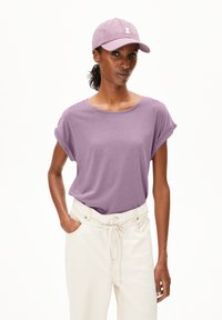 Short-sleeve lavender t-shirt with rolled cuffs, worn with high-waisted white pants featuring a drawstring and side pockets.
