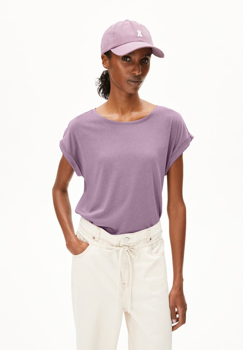 Short-sleeve lavender t-shirt with rolled cuffs, worn with high-waisted white pants featuring a drawstring and side pockets.