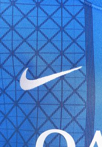 Blå treningsskjorte med et teksturert geometrisk mønster med diamanter, et hvitt Nike-logo og en glatt stoffoverflate.