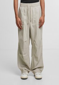 Light beige, wide-leg cargo pants made of cotton-blend fabric. Features elastic waistband, drawstring, and multiple pockets. Smooth texture.