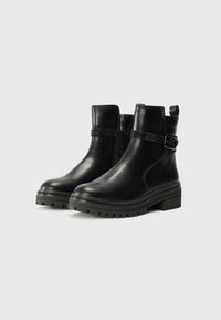 Stivali ankle neri in pelle con una cintura testurizzata e dettaglio in fibbia, chiusura con zip laterale e suola in gomma spessa e scolpita.