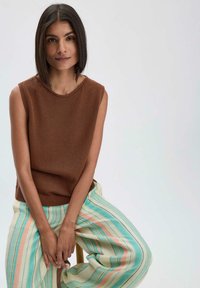 Bruin mouwloos tricot top met een ronde halslijn, gecombineerd met pastelgestreepte, luchtige broek in blauw, groen en perzik tinten.