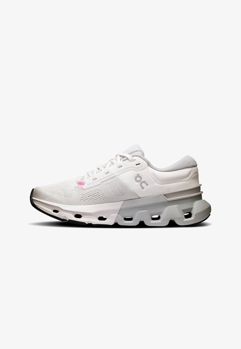 White athletic shoe with a textured mesh upper, accented with light gray and pink details. Features a thick sole with cut-out sections.