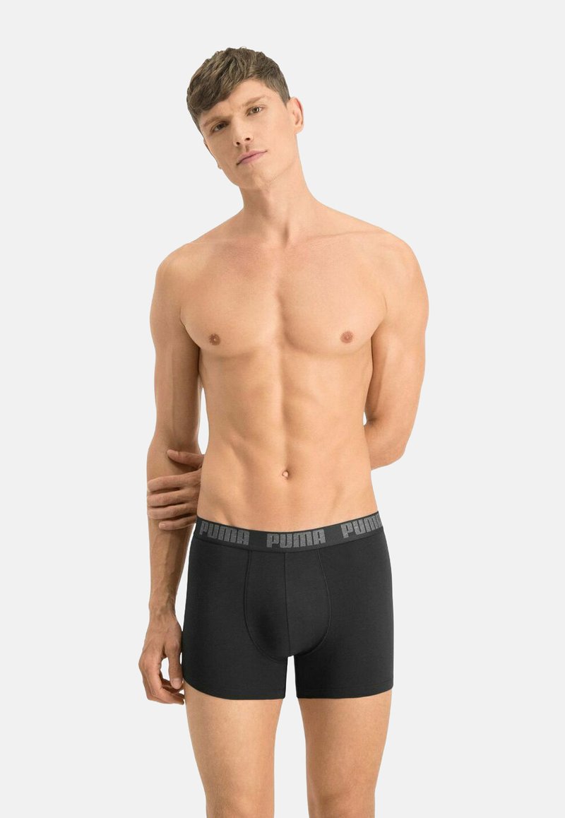 Black boxer briefs made of smooth fabric, featuring an elastic waistband with logo accents. The fit is snug with a mid-thigh length.