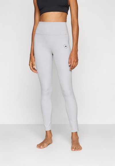 Leggings taille haute gris clair en tissu extensible, présentant un design ajusté et un petit logo près de la hanche gauche.