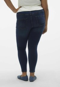 Jeans skinny azul oscuro con bolsillos traseros, que presentan un acabado suave y un ajuste ceñido, combinados con zapatos planos azul claro.