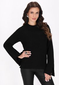 Pulover tricotat negru, cu mâneci lungi și decolteu tip crew. Are manșete evazate și o țesătură texturată. Este asortat cu pantaloni negri.