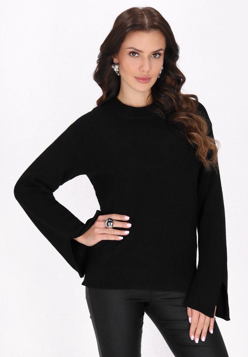 Pulover tricotat negru, cu mâneci lungi și decolteu tip crew. Are manșete evazate și o țesătură texturată. Este asortat cu pantaloni negri.