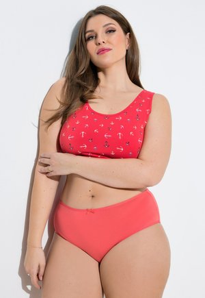 Donna con capelli castani lunghi che indossa una canotta rossa con stampe di ancore e mutandine corallo a vita alta su uno sfondo bianco.