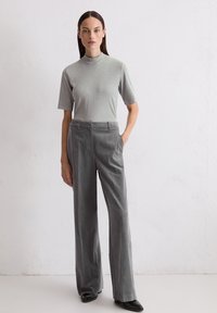 Jasnoszara, dopasowana bluzka z stojącym kołnierzem w parze z szarymi spodniami o wysokim stanie i szerokich nogawkach. Płaskie buty dopełniają elegancki, minimalistyczny design.