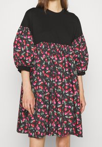 Czarna bawełniana bluzka z bufiastymi rękawami, kontrastująca z wzorzystą spódnicą w kwiaty, z wiśniami i liśćmi na ciemnym tle. Zwiewny fason sukienki.