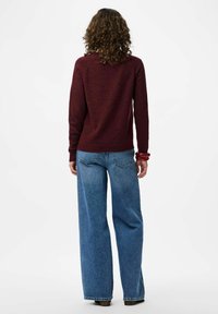 Bordo pulover z dolgimi rokavi, v kombinaciji z širokimi modrimi kavbojkami. Tekstura se zdi mehka, s sproščenim krojem in minimalnimi detajli.