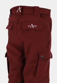 Burgunderrøde cargobukser lavet af blødt stof, med sidelommer, et mærke på bagsiden og diskrete syningdetaljer.