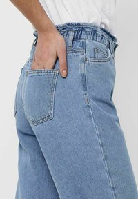 Light blue denim jeans with an elastic waistband and one back pocket. The fabric has a soft texture and features subtle stitching details.