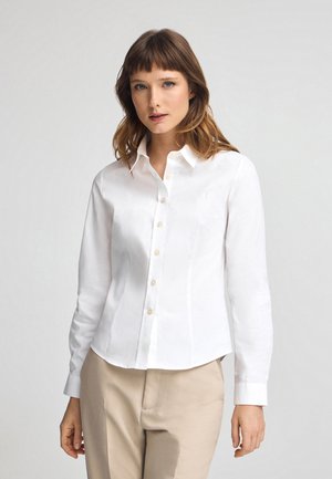 Witte overhem shirt met lange mouwen, slim fit, en een subtiel geborduurd logo op de linkerborst. Glad materiaal en manchet met knopen.