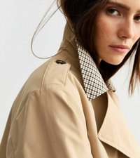 Beige trenchcoat med detaljer i kollar med rutig mönstring. Tyget verkar vara slätt med en strukturerad form och en enda knapp på axeln.