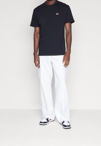 Czarna bawełniana koszulka z okrągłym dekoltem, z niewielkim wielokolorowym logo. W połączeniu z białymi szerokimi spodniami i czarnymi tenisówkami.