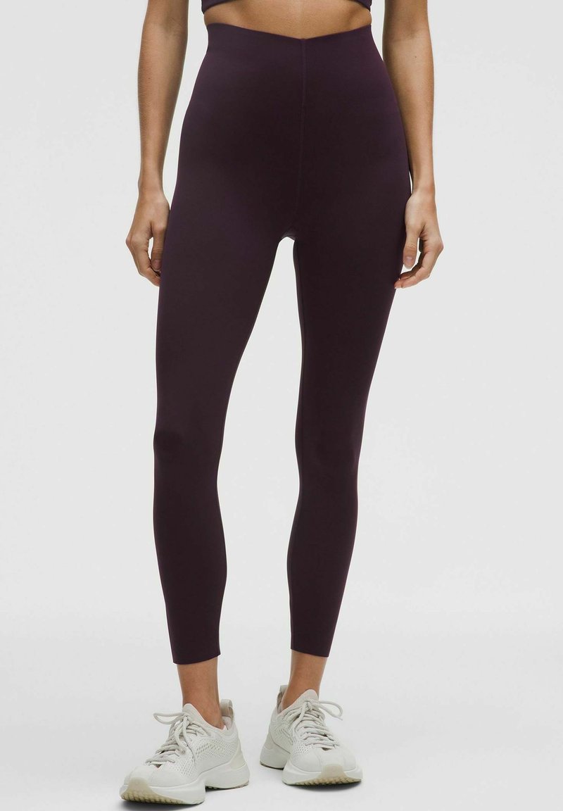 Aukštu liemeniu purpurinės tamprės iš lygaus tamprios medžiagos, siaurėjančios formos, su siūlės detale. Derinamos su šviesiai pilkais sportbačiais.