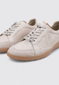 Zapatillas de ante beige claro con puntera perforada, cordones grises y suelas de goma. Presentan un logo discreto en el lateral y un acento naranja en la lengüeta.