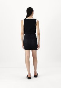 Černý top bez rukávů s bílým lemem, zkombinovaný s dobře padnoucí černou džínovou sukní s rozparkem na zadní straně a dvěma zadními kapsami. Černé platformové boty.