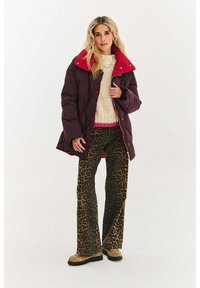 Kasztanowy puchowy płaszcz z czerwonym kołnierzem, kremowy sweter z dzianiny oraz brązowe, poszerzane spodnie w panterkę. Materiały o fakturze, widoczne guziki.