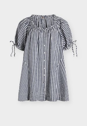 Vestito corto a maniche corte in tessuto vichy bianco e nero con bottoni frontali, scollo arricciato e polsini delle maniche annodati su sfondo semplice.