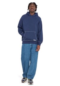 Navy blue hoodie with a front pocket, raglan sleeves, and contrasting white stitching, paired with loose-fit, light blue denim jeans.