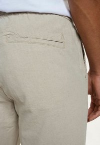 Lichtbeige linnen broek met een gladde textuur, voorzien van een achterzak en minimalistische stikdetails op de tailleband.