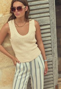 Beige kammitud top, millel on avatud kaelus, koos helesiniste ja valgete triibuliste laia säärega pükstega. Üks suurte prillidega ja lihtne kaelakee.