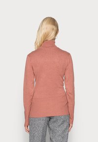 Maglione a maniche lunghe, con collo alto color rosa polveroso, dalla texture a costine e dalla vestibilità aderente. Orlo posteriore decisamente più lungo con fessure laterali.