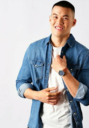 Denim shirt, white T-shirt, and brown leather strap watch with blue dial. Short sleeves, button-down design, casual fit. White background.