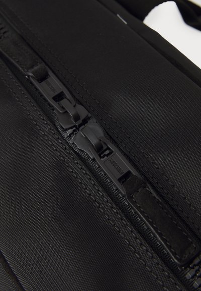 Geantă din material textil negru, cu o suprafață netedă și texturată, prezentând un fermoar solid tot negru, care evidențiază mecanismul fermoarului și cusăturile rezistente.