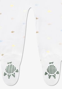 Άσπρες κάλτσες με πολύχρωμα λογότυπα Lacoste σε κίτρινο, μπλε και καφέ. Οι σόλες έχουν πράσινες κουκκίδωτες λαβές και σχέδιο χελώνας.