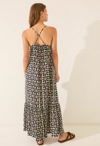 Abito maxi nero con un motivo geometrico bianco e dettagli rossi. Presenta spalline incrociate regolabili e un orlo a volant a strati.