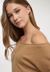 Maglione beige a spalle scoperte realizzato in tessuto morbido e strutturato, con scollo ampio e vestibilità rilassata, con sottili coste lungo i bordi.