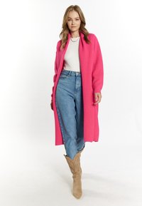 Lång, öppen kardigan i strålkastande rosa ribbat stickat, kombinerad med ljusblå högmidjade jeans och bruna cowboystövlar med intrikata sömmar.